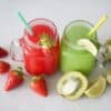 Two Smoothies one red one green in glasses side by side with straws surrounded by strawberries and kiwis