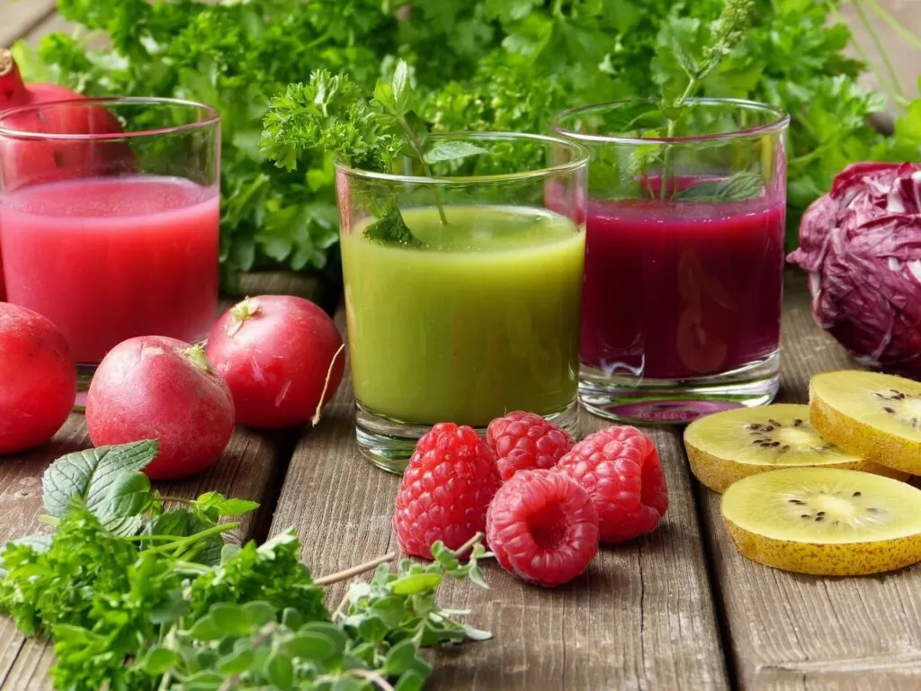 Green and red smoothies surrounded by fruits and vegetables