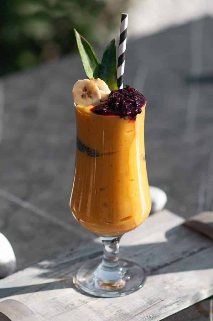 A Banana Smoothie in a tall glass with fruit in the glass with a straw.