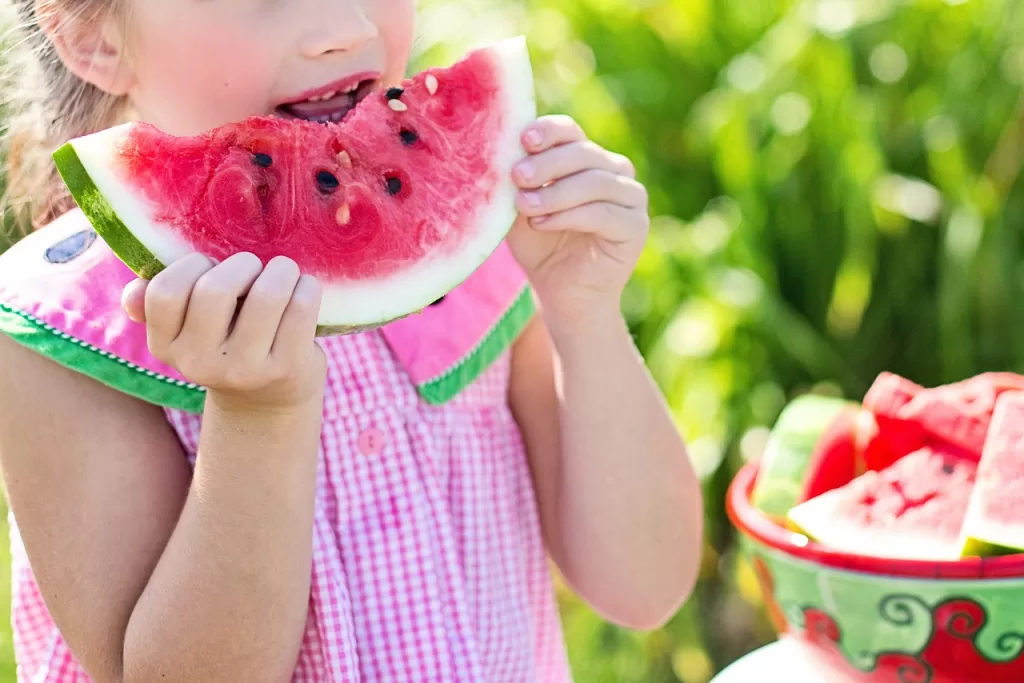 Little girl wearing pink eating a slice of watermelon.