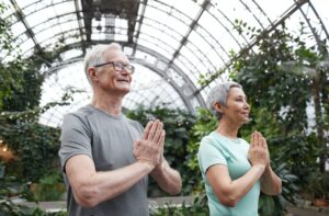 A man and a woman standing side by side palms clasped together in meditation.