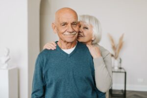 A woman standing behind her man smiling with her arm wrapped around him.