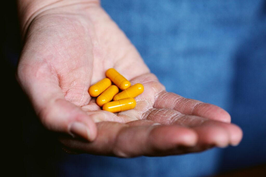 A hand holding five yellow natural supplement capsules.