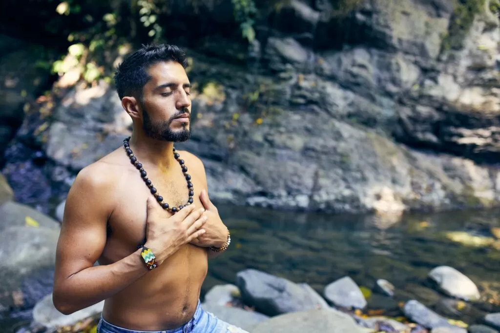 A man sitting with his eyes closed and his hands crossed pressed to his chest.