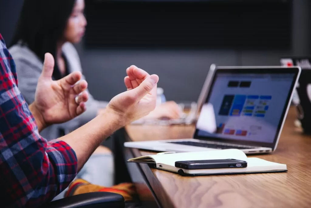 People talking with hand gestures at a desk in front of a laptop.