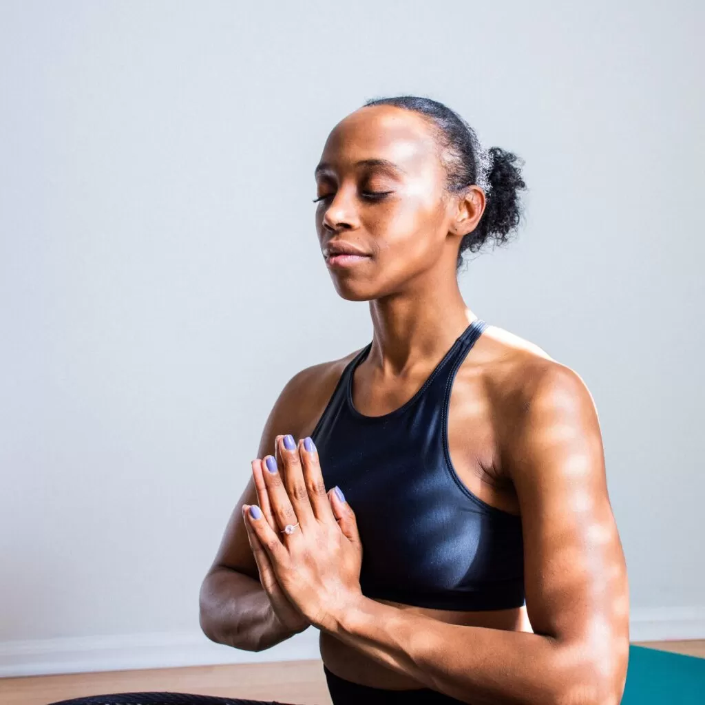 A woman sitting on the floor with her eyes closed and hands clasped practicing mindfulness meditating.