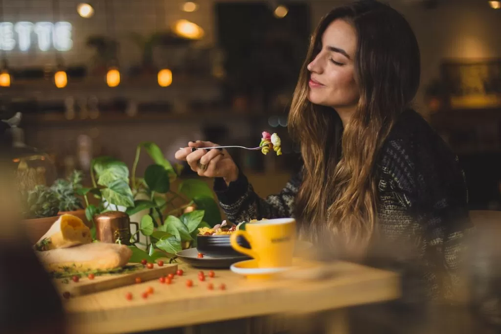 A woman holding a fork with food and her eyes are closed.