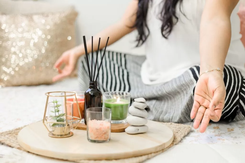 A woman sitting in a crossed leg yoga position with mindfulness tools incense and candles.