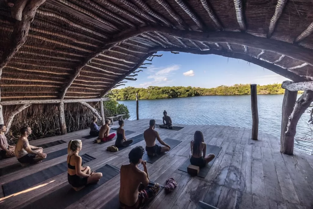 A group of men and women facing the seashore meditating.