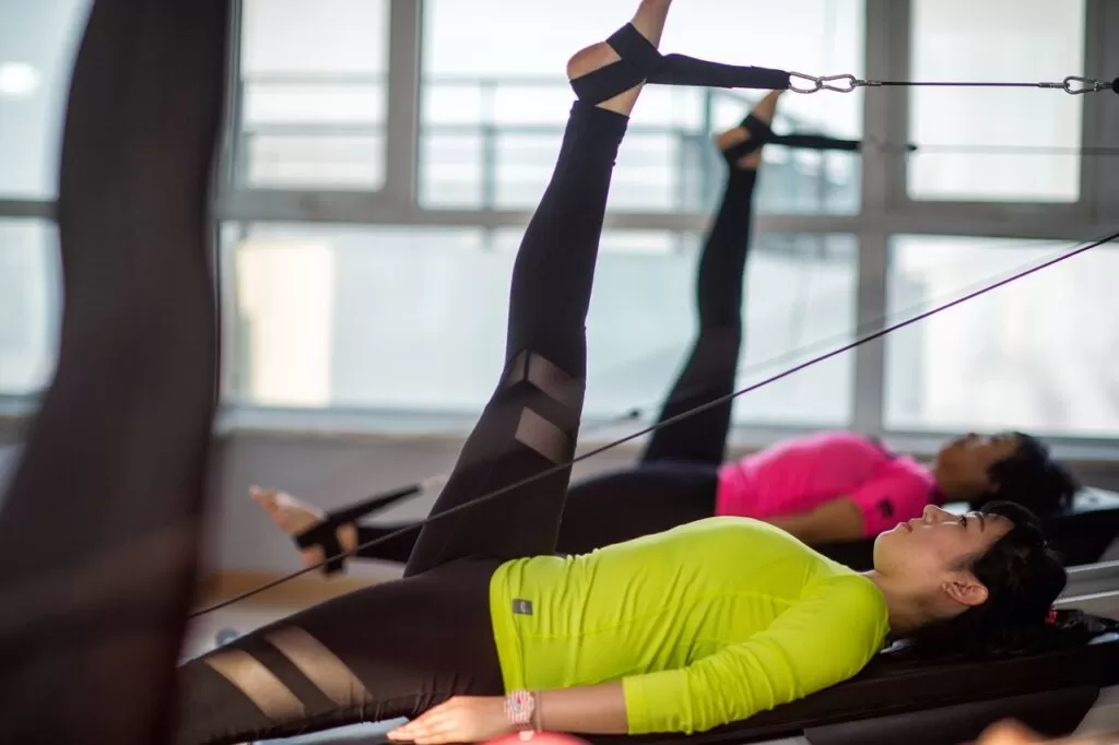 Two girls doing Pilates leg lifts on fitness equipment,