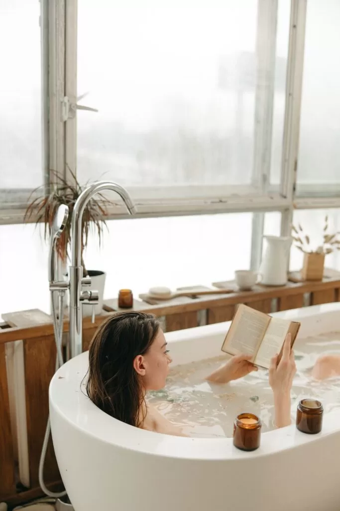 A woman reading a book while taking a bath.