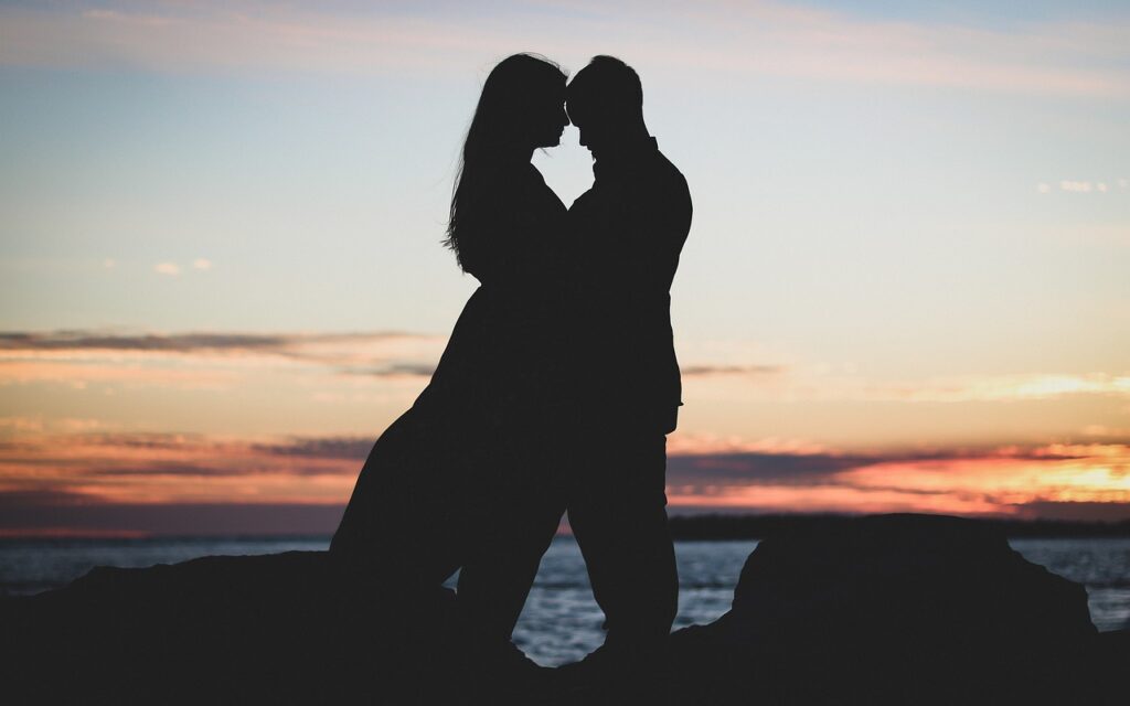 A couple met using the law of attraction on the beach sunset hugging each other and staring into each others eyes.