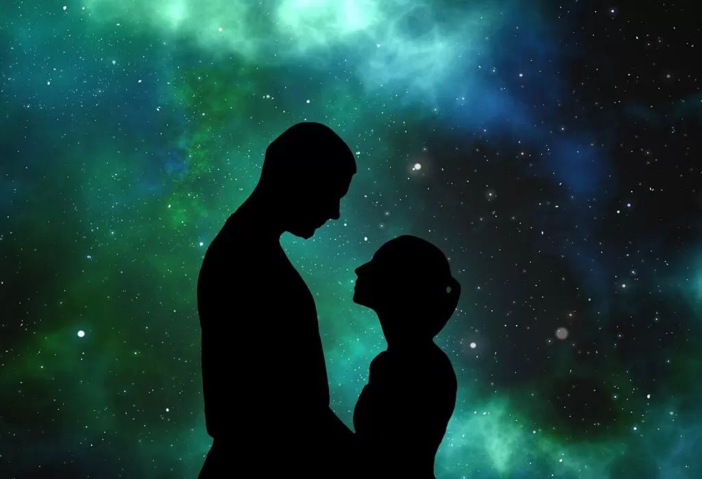 The Law of Attraction brings a man and a woman black silhouette facing one another on a green universe background.