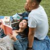 A man and a woman out side on a blanket reading books.