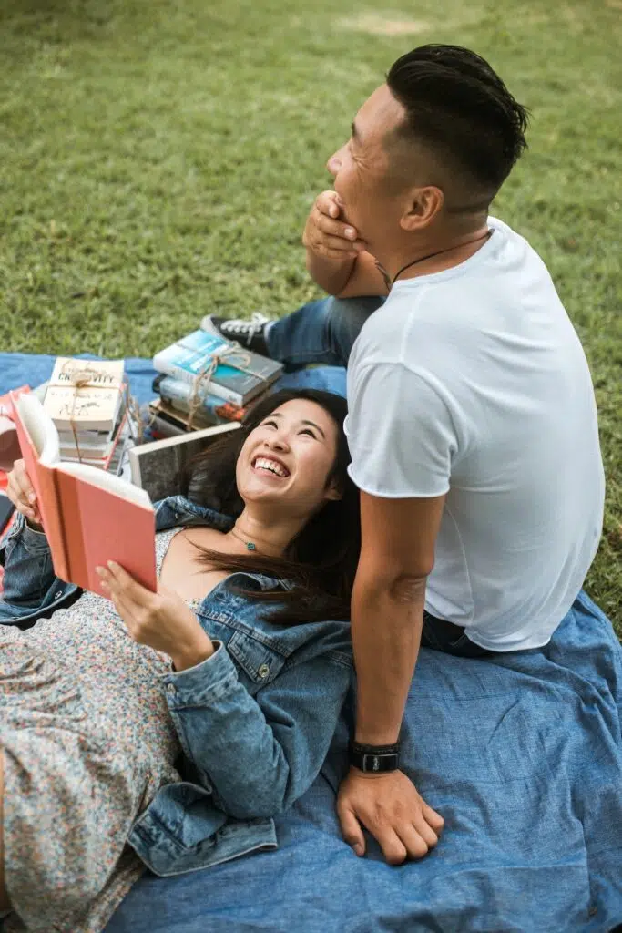 A man and a woman out side on a blanket reading books.
