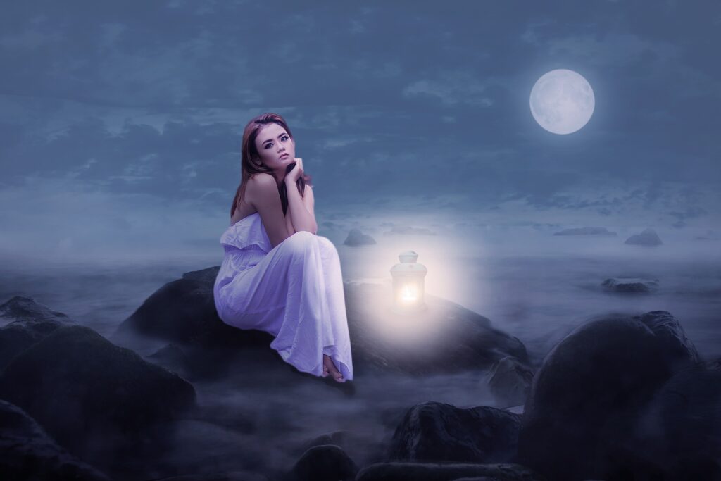 A woman sitting at night staring at a full moon.