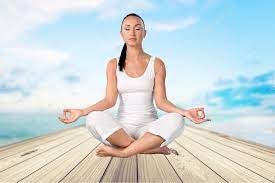 Woman dressed in white sitting on a pier in the lotus yoga position.