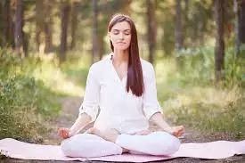 Woman with legs crossed sitting in the woods in a yoga position.