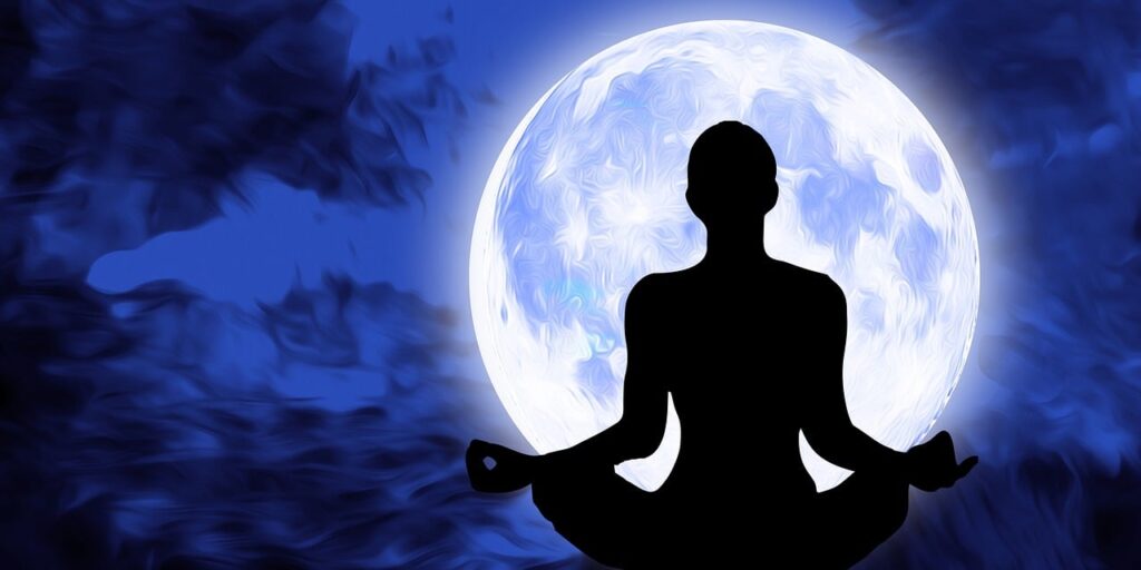 A woman sitting in a yoga position in front of a bright full moon manifesting with the law of attraction.