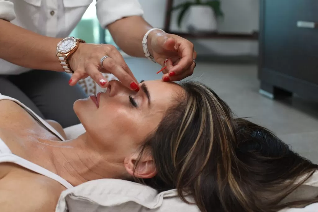 A women receiving holistic health and wellness laying on her back getting a facial massage.