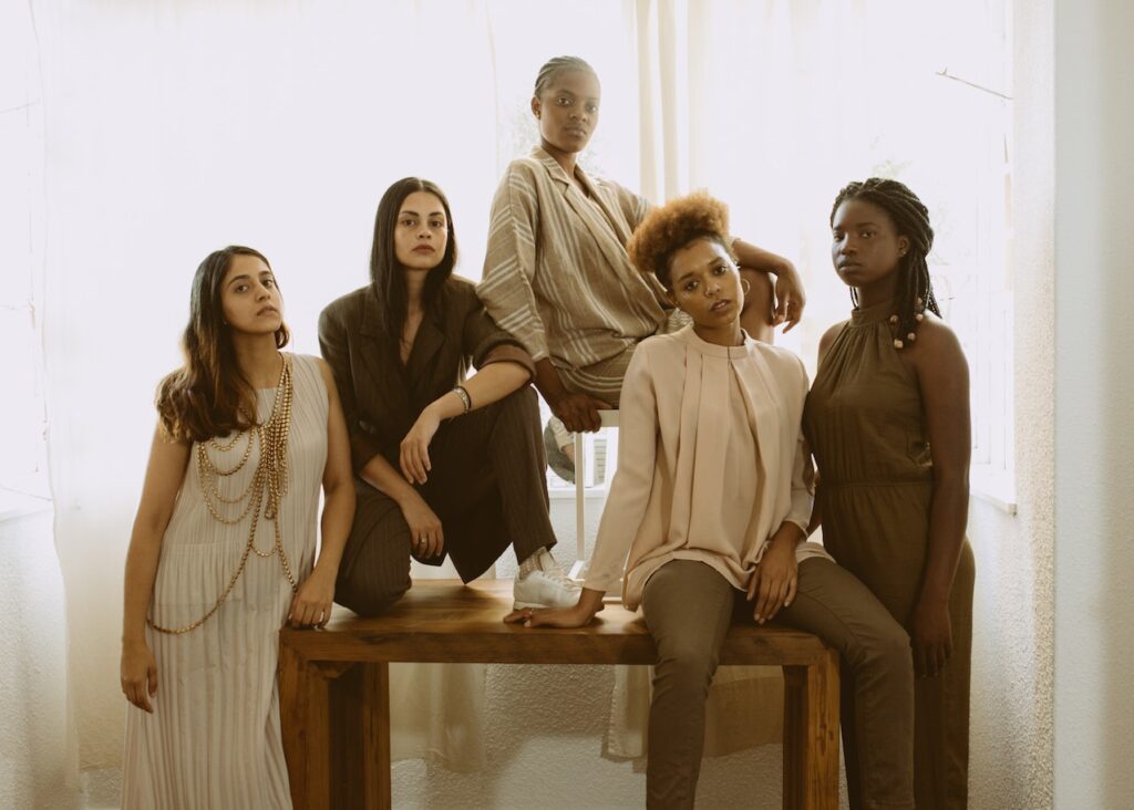 Five women standing tall and proud dressed in browns and black.