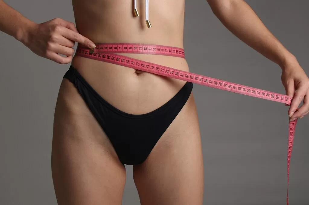 A woman measures her waist and weight loss with a tape measure.