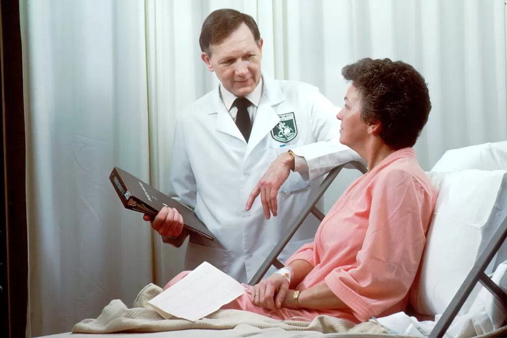 A doctor talking to a patient about cardiovascular diseases in white coat holding a black tablet computer.