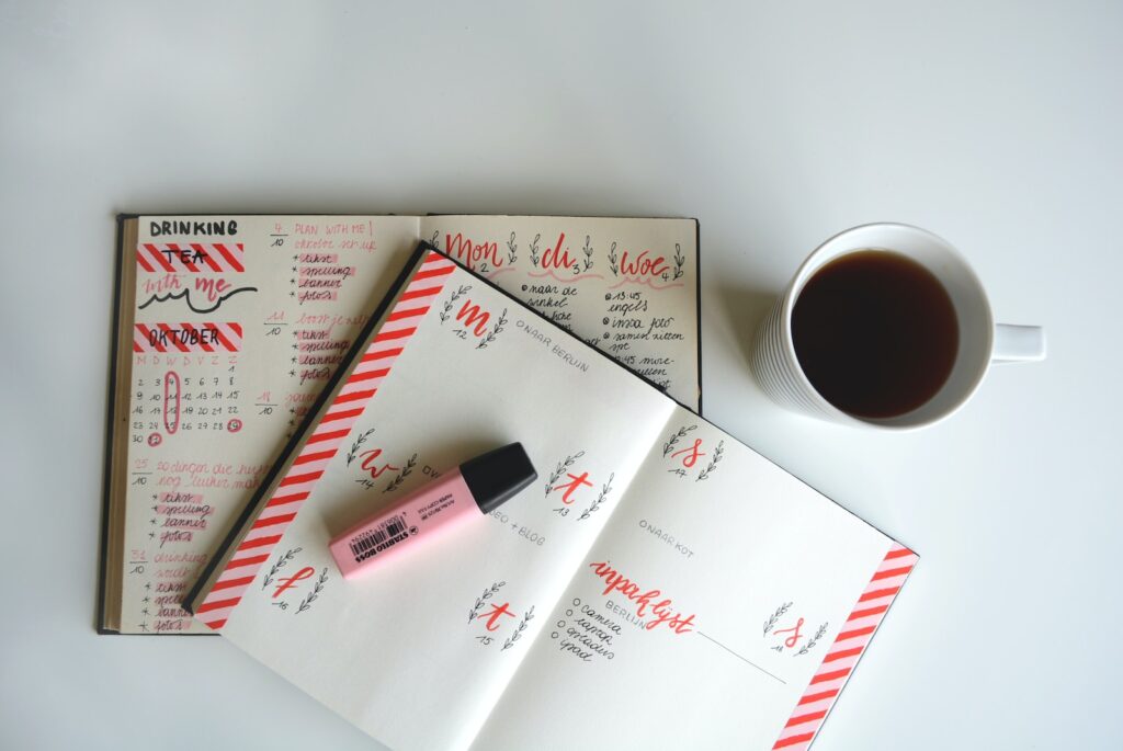 white ceramic teacup with beverage beside pink marker beside a diet planning booklet.