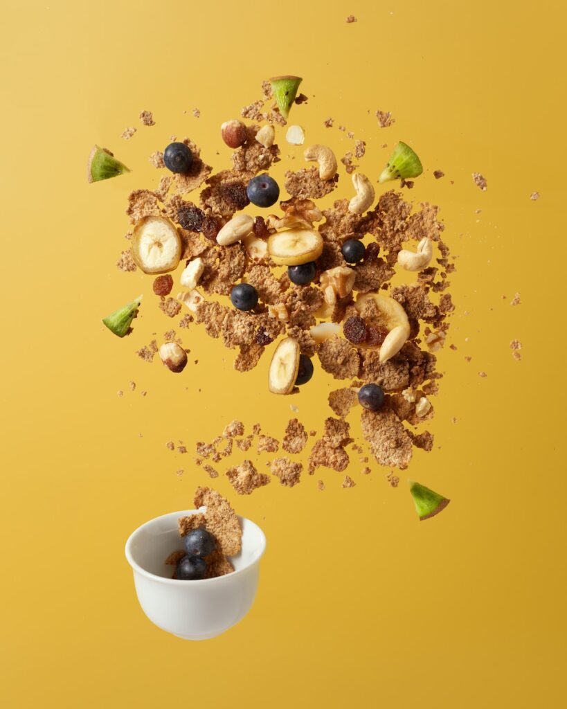 brown nuts and grains tossed into the air in white ceramic bowl