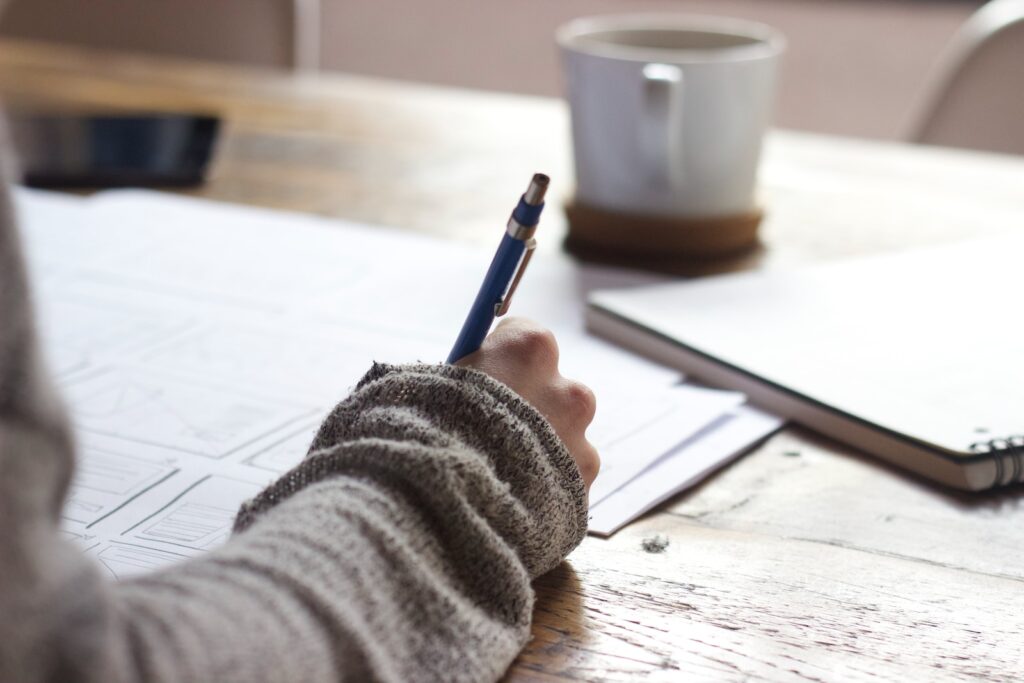 person writing dietary guidelines in a brown wooden table near white ceramic mug